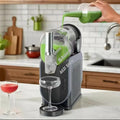 A grey slushie maker on a kitchen counter, with green liquid being poured into the clear mixing chamber.