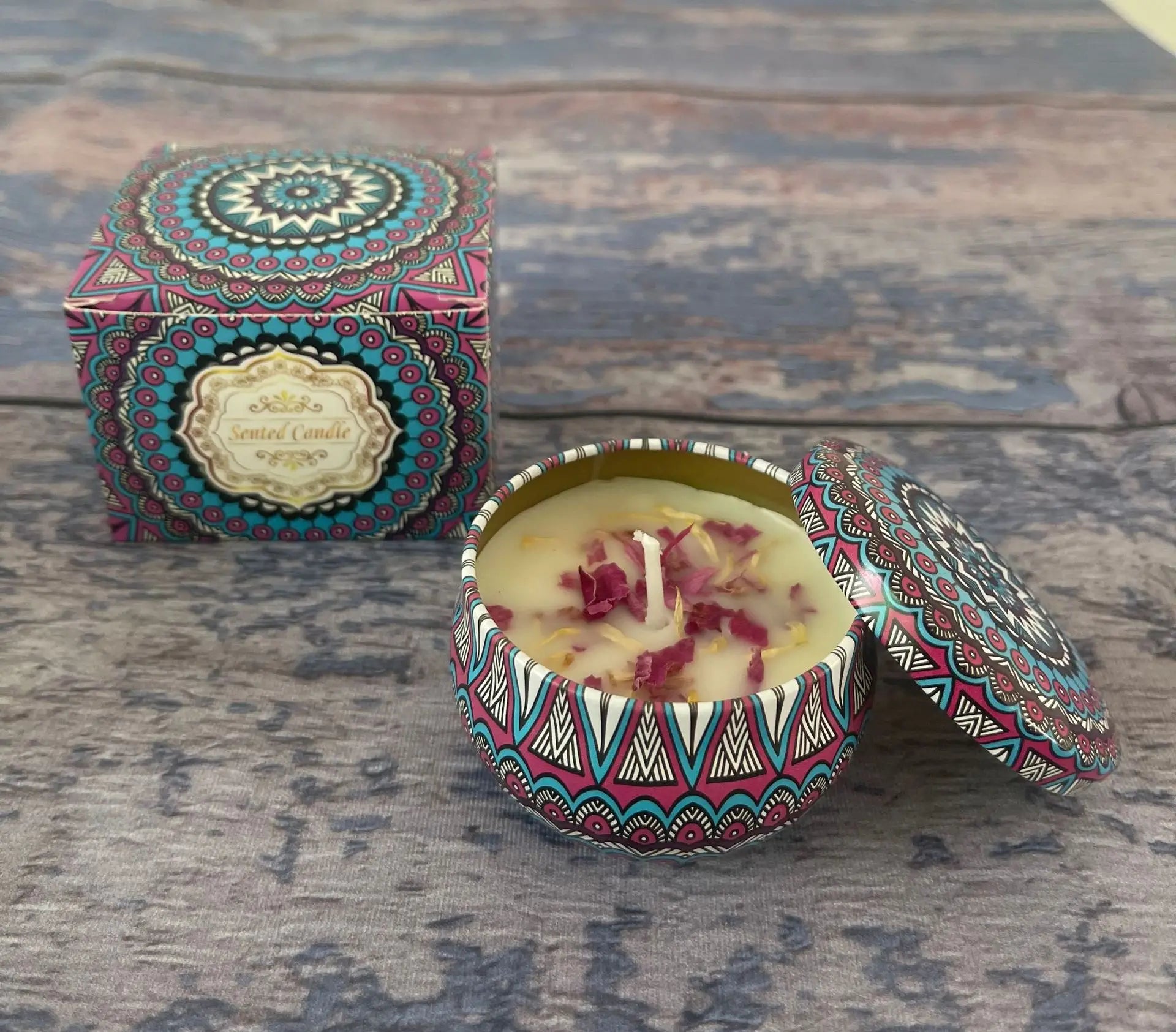 Scented candle in a colourful mandala-patterned tin with its matching box, topped with dried flower petals.