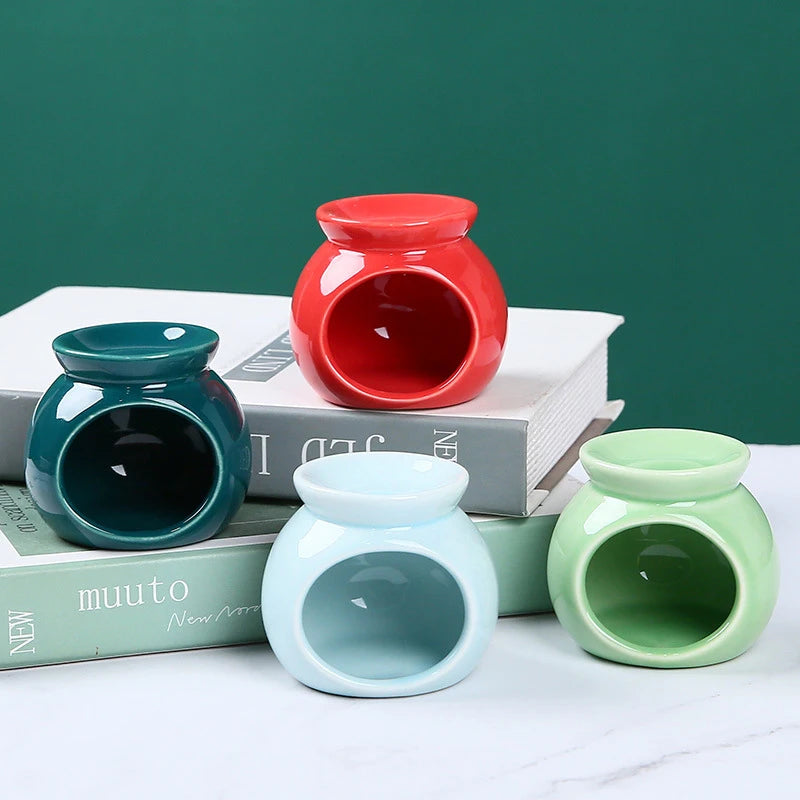 Four round, glossy ceramic oil burners in red, dark teal, light blue, and sage green arranged on top of books.