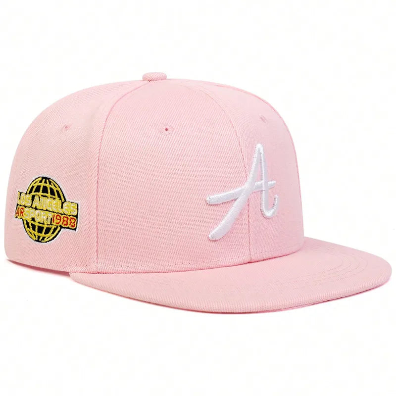 Pastel pink unisex baseball cap with white embroidered 'A' on the front and a yellow globe emblem on the side.