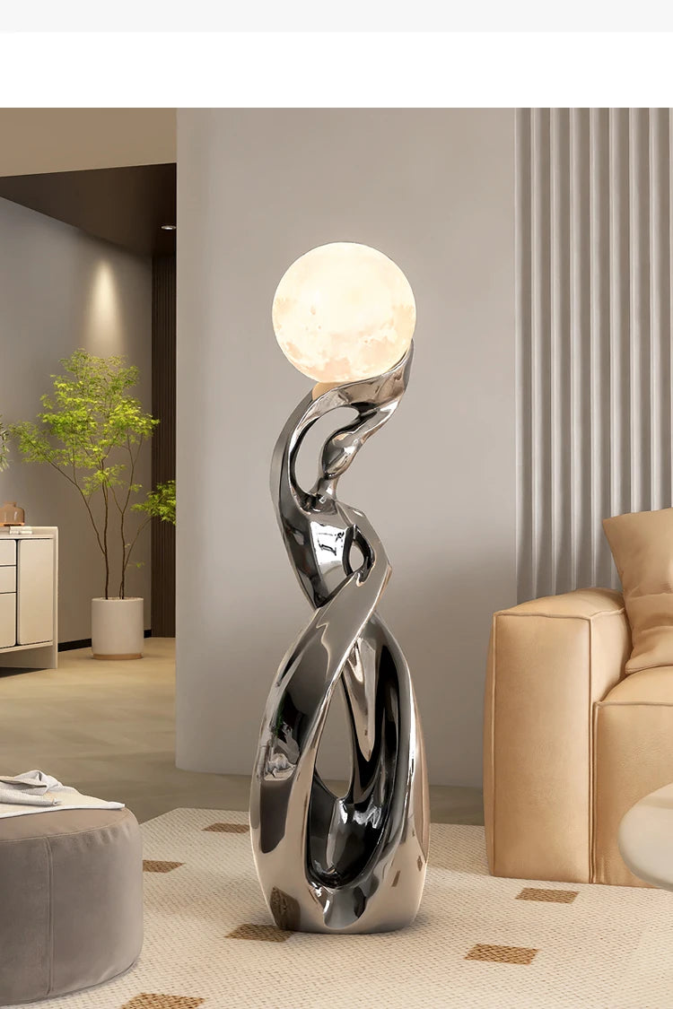 Tall, abstract silver resin floor statue featuring a glowing, moon-like sphere topper in a modern living room setting.