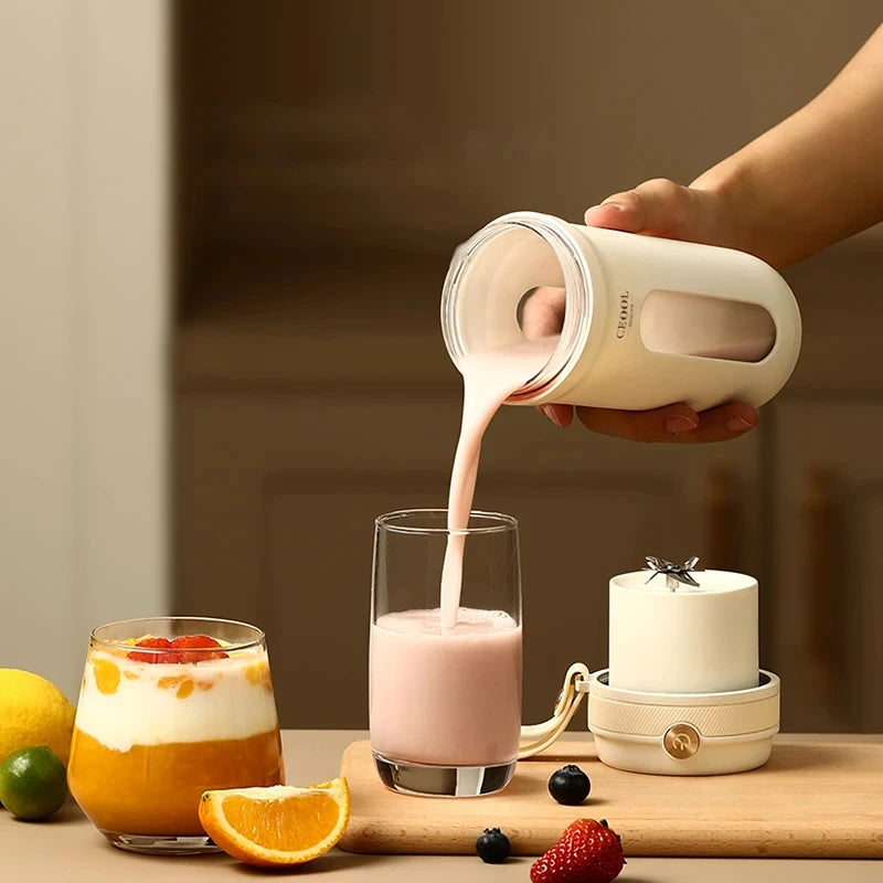 A hand pours a pink smoothie from a minimalist, cream-colored portable blender into a glass on a wooden board.