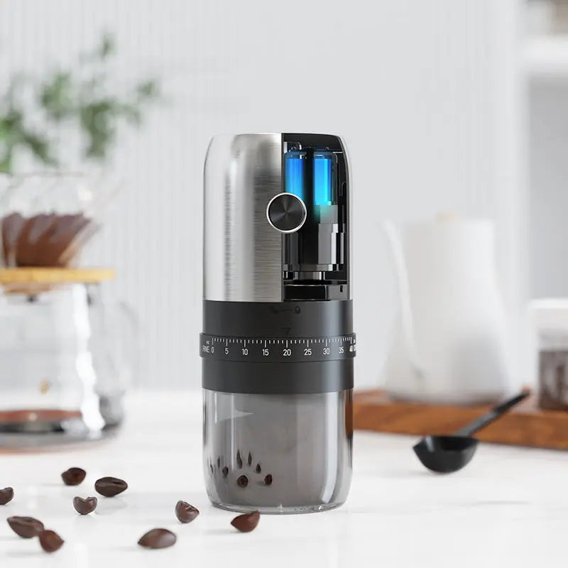 Modern portable coffee grinder with brushed silver top, matte black base, numbered dial, and clear catch cup on table.