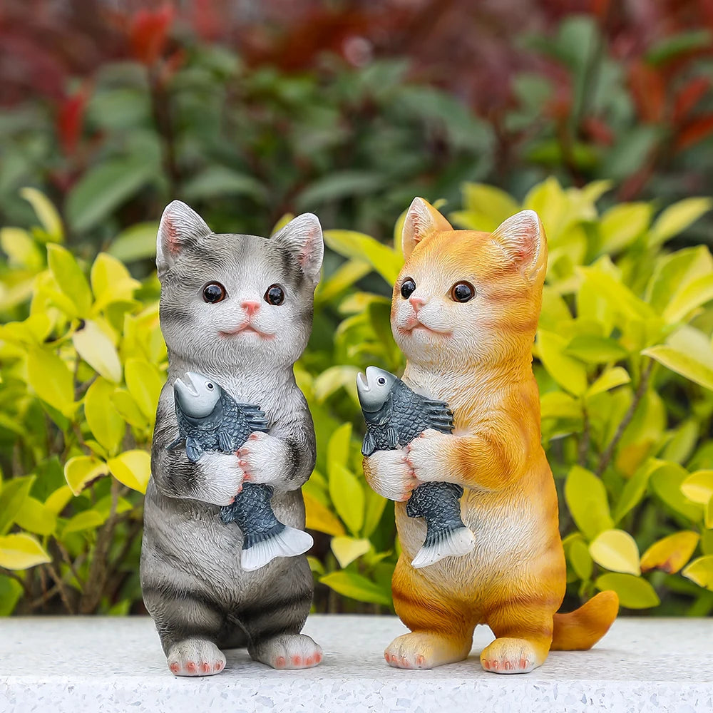 Two charming resin cat statues, one orange and one grey tabby, each standing and holding a grey fish.