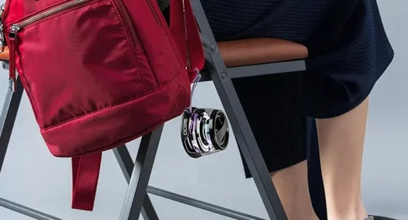 Portable black Bluetooth speaker with RGB lighting and phone holder, hanging from a red backpack.