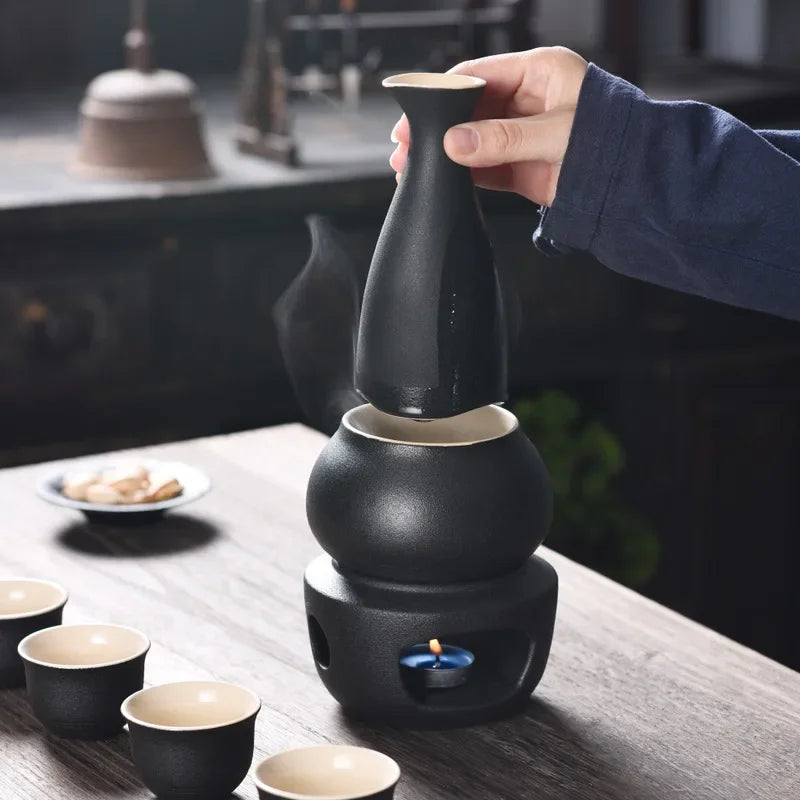 Matte black ceramic sake set with warmer, candle stove, and four matching cups on a wooden table.