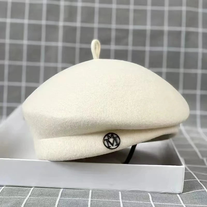 Cream wool felt beret with a small top loop and a circular metallic detail on the brim.
