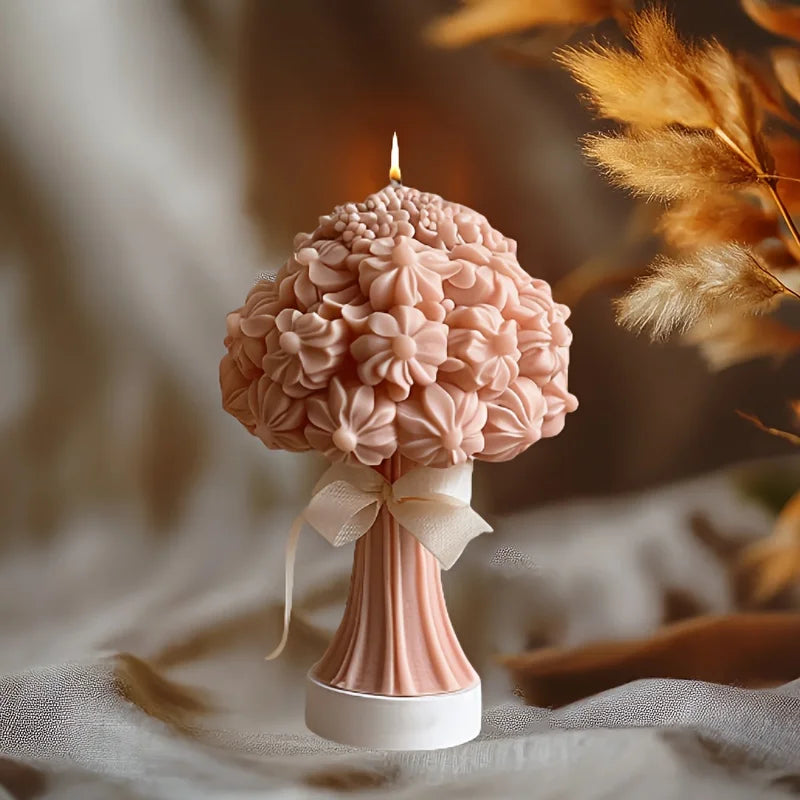Dusty pink floral bouquet candle shaped like a tree with a lit wick and cream ribbon tied around the stem.