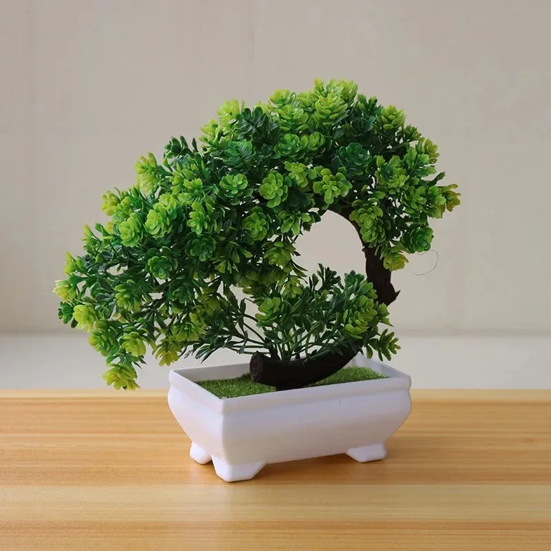 Artificial green bonsai tree with a circular, curved branch in a rectangular white pot on a wooden surface.