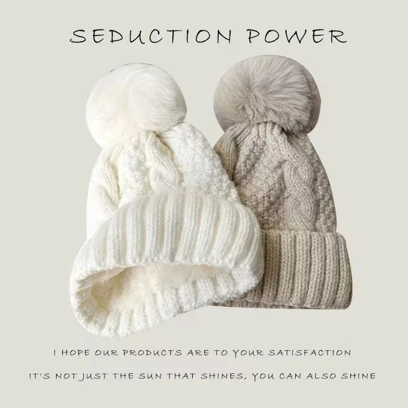 Two cable-knit winter beanie hats with pom-poms in white and beige, featuring ribbed turn-up hems.