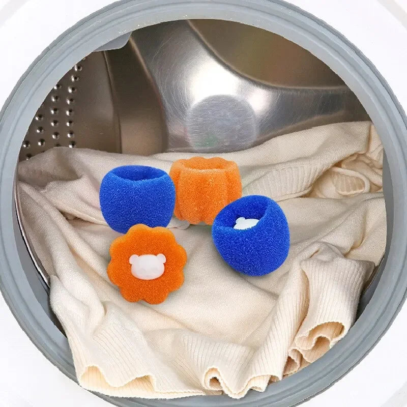 Blue and orange sponge lint catcher balls with bear icons, shown inside a washing machine drum with white clothing.