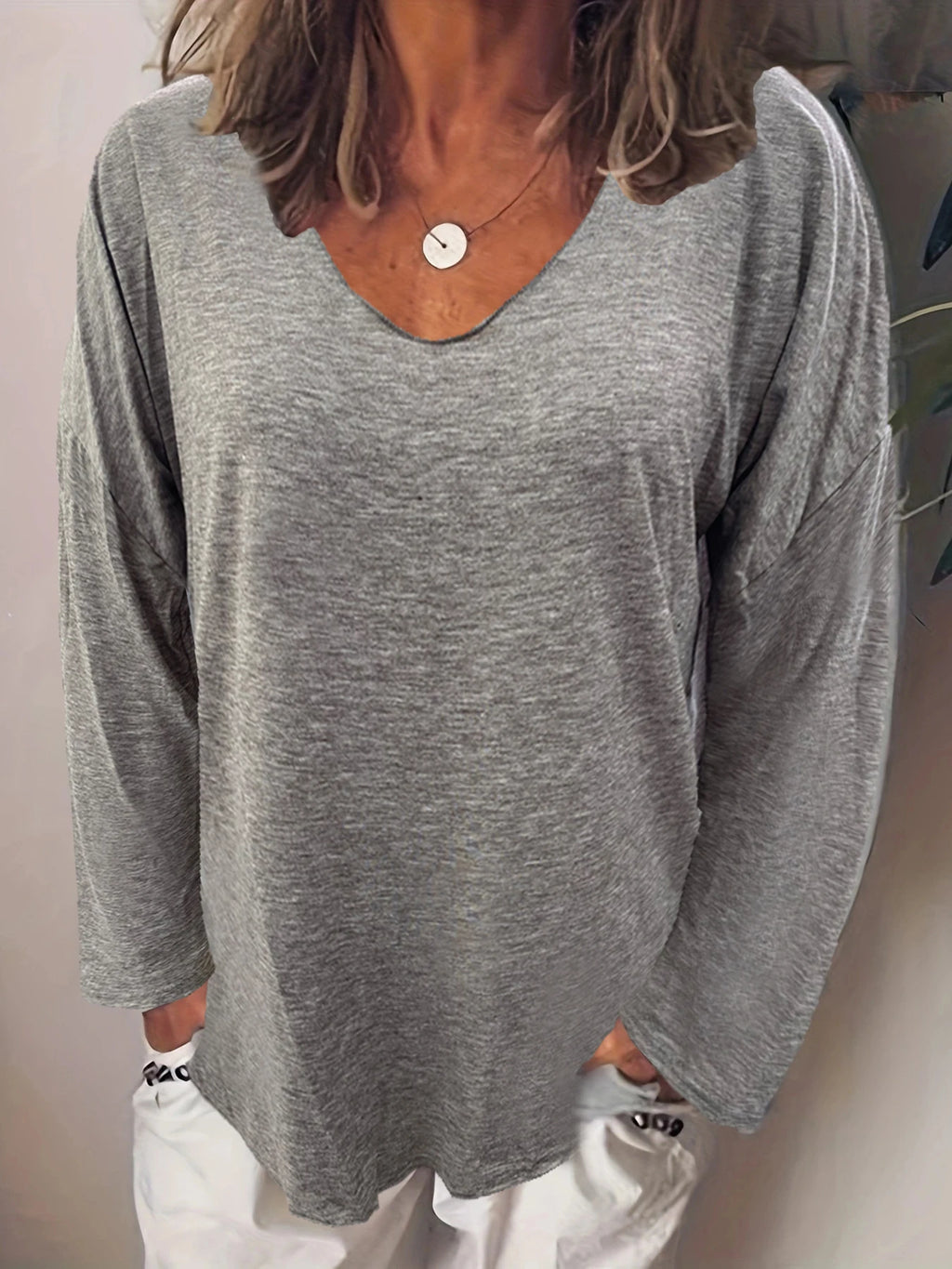 Grey long-sleeve top with a relaxed fit, drop shoulders, and a wide V-neckline. Soft, lightweight fabric.