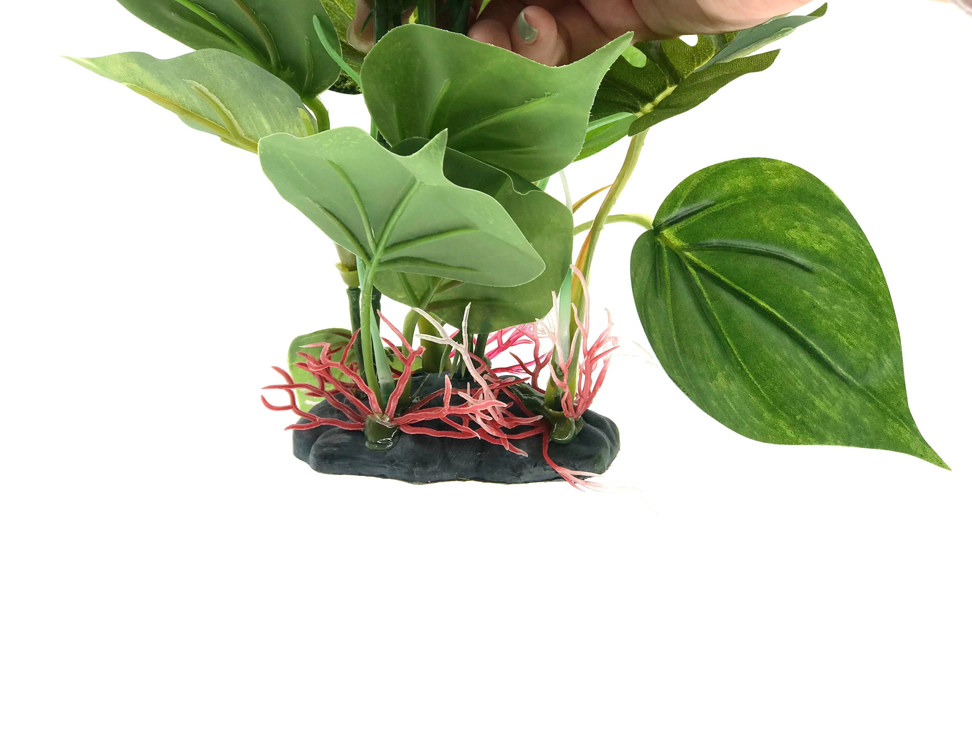 Artificial aquarium plant with large green leaves and red roots, set on a dark, weighted base against a white background.