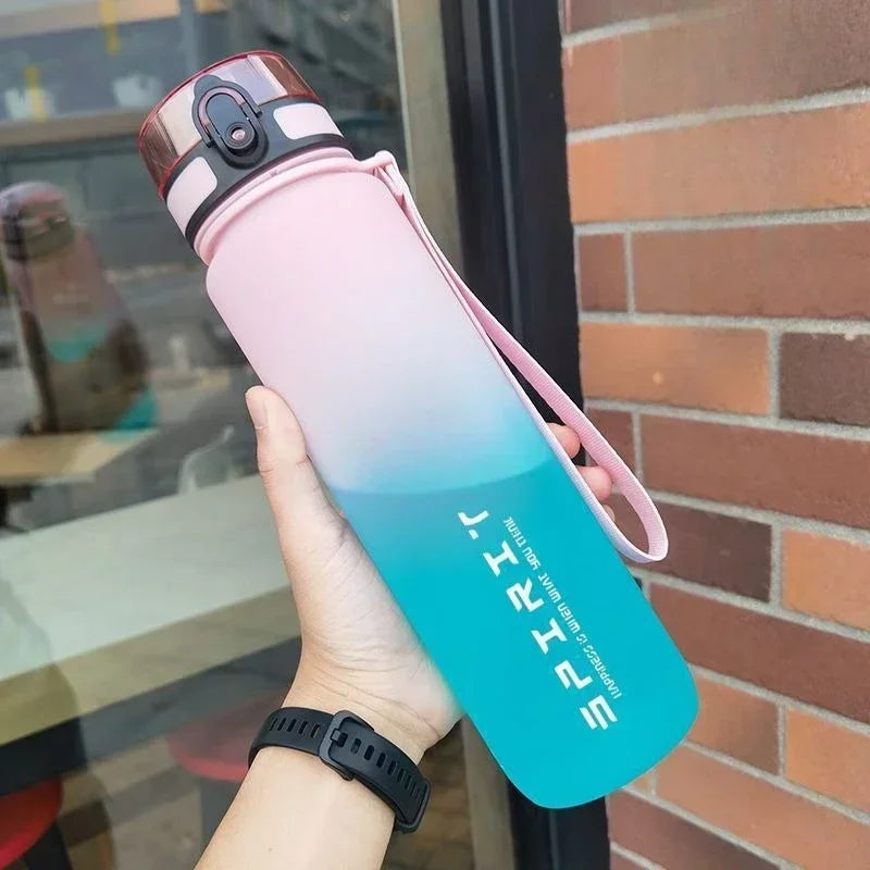 A hand holds a pink-to-blue ombre water bottle with a black flip-top lid, carry strap, and "SPIRIT" text.