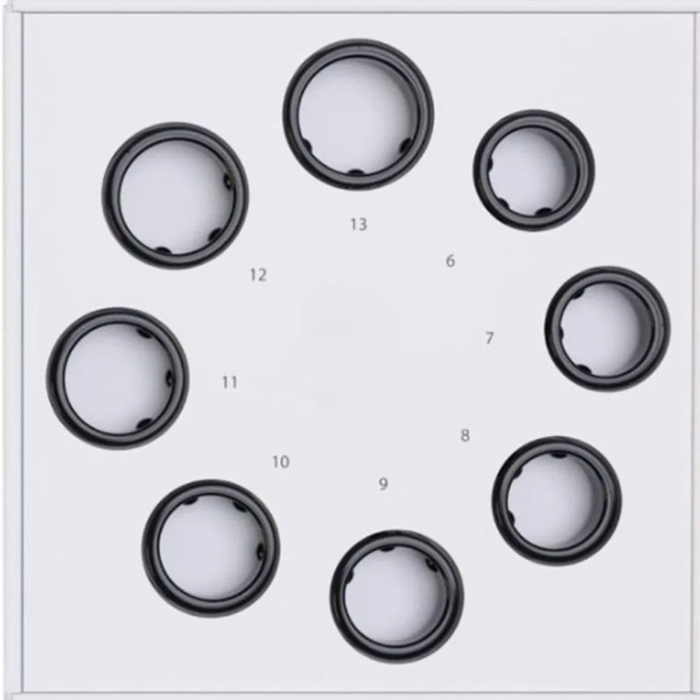 A set of black smart health rings arranged in a circle on a white display tray, marked with various UK ring sizes.