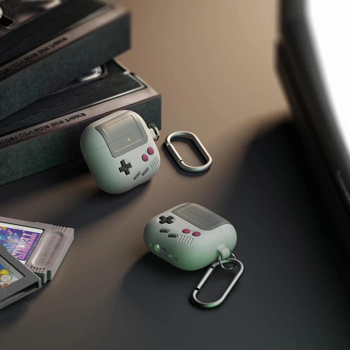 Retro game console-style AirPods case in pale green silicone with a metal carabiner clip.