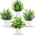 Four small artificial green plants in rounded white pots, featuring varied leaf styles on a plain white background.