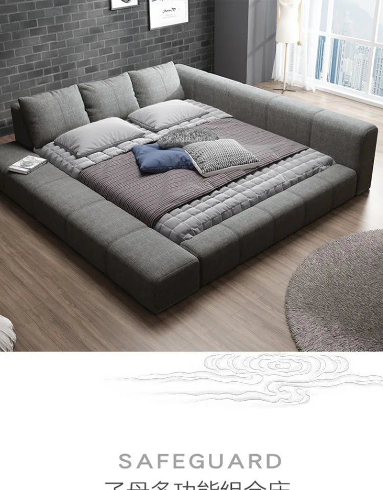 Modern grey fabric double bed with a low-profile padded frame and integrated headboard, styled with soft furnishings.