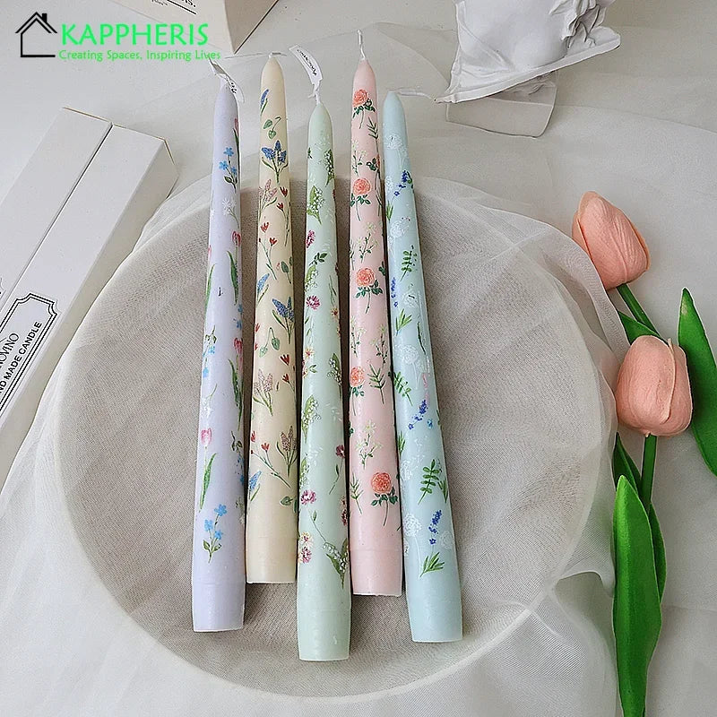 Five pastel-coloured tapered dinner candles featuring delicate floral patterns on a white plate with tulip accents.