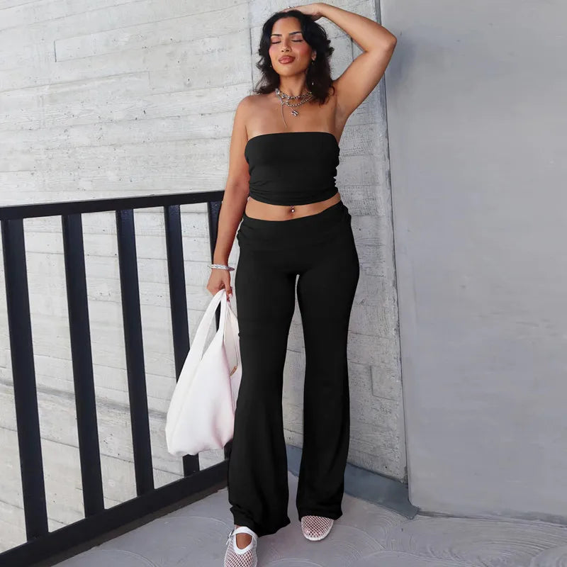 Model wearing a black strapless crop top and matching high-waisted flared trousers, holding a white bag.