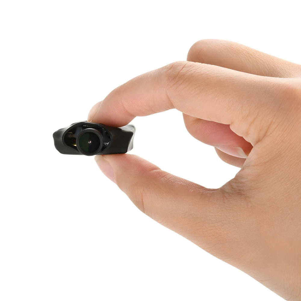 A hand holding a tiny, black, plastic miniature camera module against a white background.