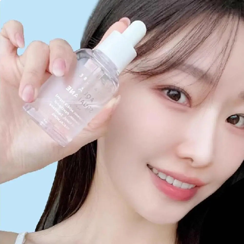 Smiling woman holding a clear glass bottle of facial serum with a white dropper cap against a light blue background.