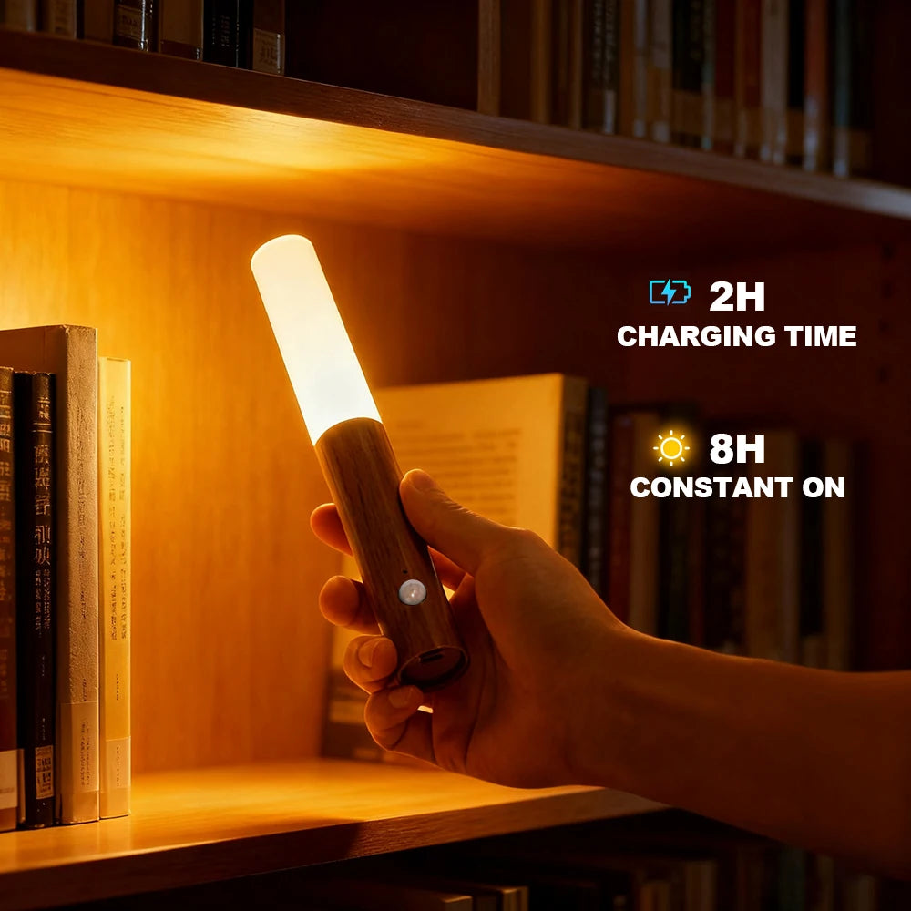 A handheld, wood-effect motion sensor LED night light glowing with warm light, held in front of a wooden bookshelf.