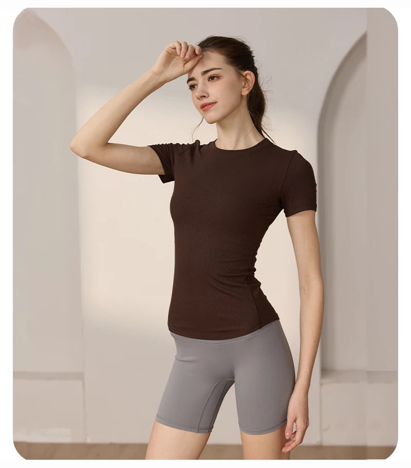 Woman wearing a dark brown, short-sleeve ribbed gym t-shirt paired with grey tight athletic shorts.