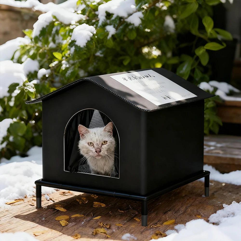 A black, waterproof outdoor cat house on legs, sheltering a cat in a snowy garden setting.