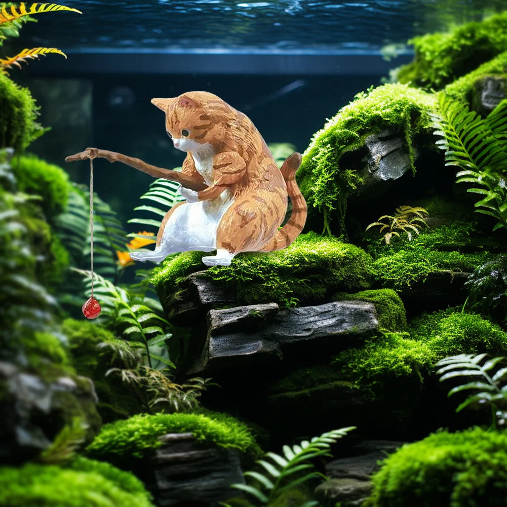 Cute ginger tabby cat aquarium ornament sitting on a mossy rock, holding a fishing rod with a red float.