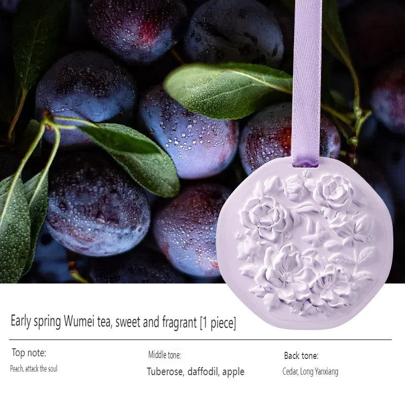 Light purple wax tablet air freshener with floral relief design and hanging ribbon against dark plums.