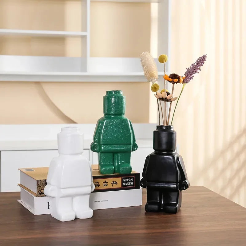 Three glossy, figure-shaped ceramic vases in white, green, and black, displayed on a wooden table.