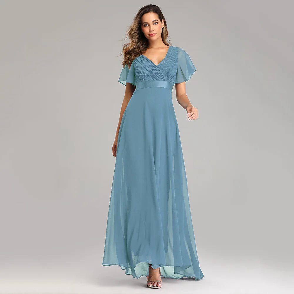 Model wearing a dusty blue chiffon maxi dress featuring a V-neck, pleated bodice, and short flutter sleeves.