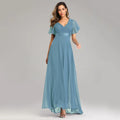 Model wearing a dusty blue chiffon maxi dress featuring a V-neck, pleated bodice, and short flutter sleeves.