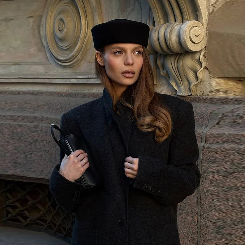 Elegant black wool Hepburn-style bucket hat worn by a woman in a dark coat, featuring a flat-top structured design.