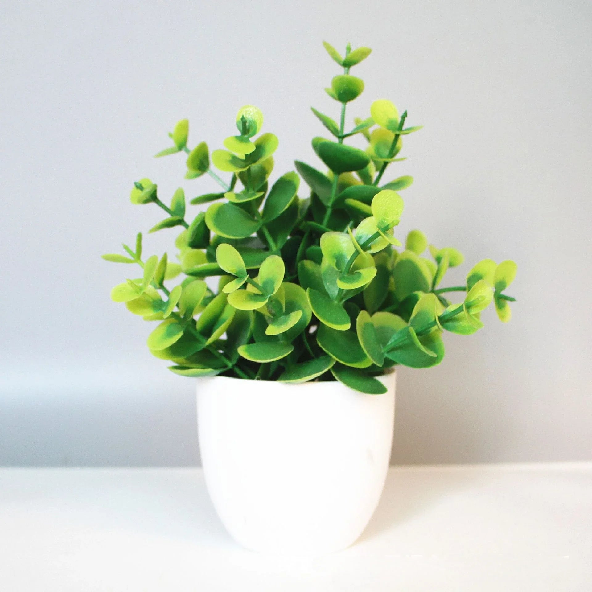 Small, bushy artificial plant with vibrant green, rounded leaves in a simple white ceramic pot.