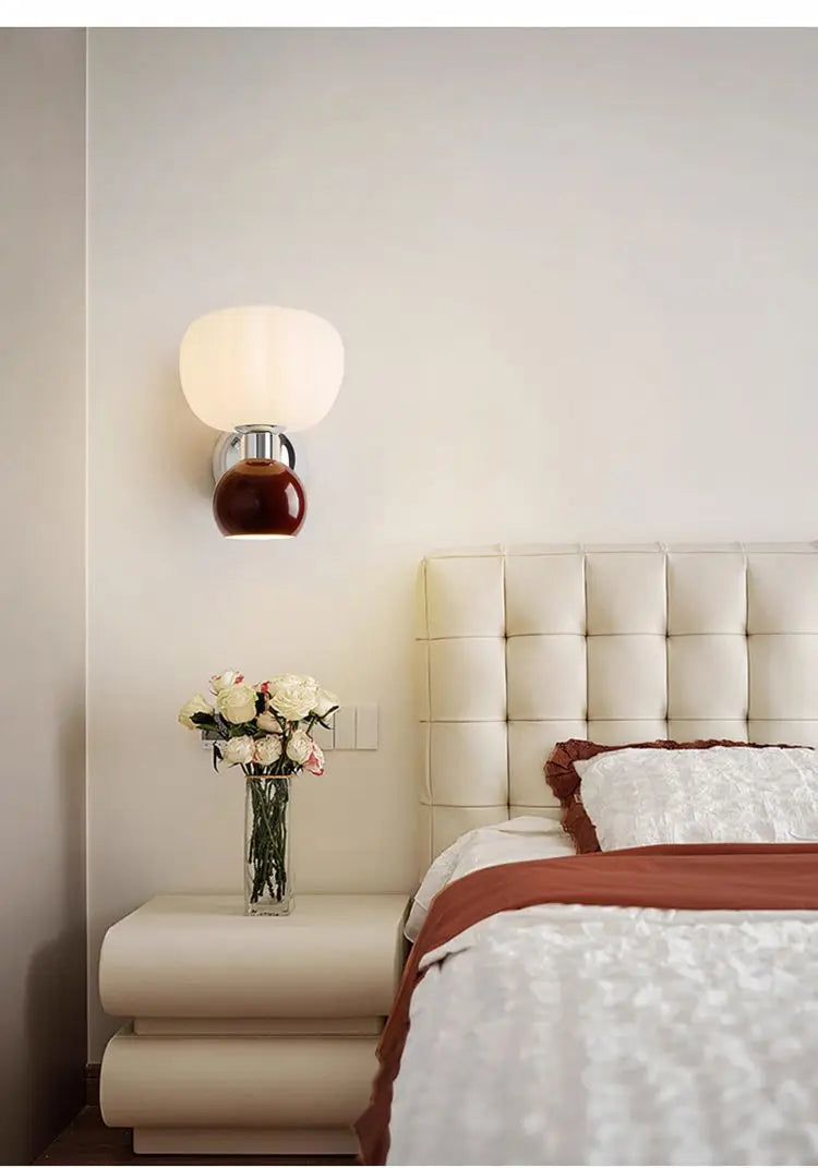 A cream and chocolate brown, double-headed wall light mounted above a bedside table in a modern bedroom.