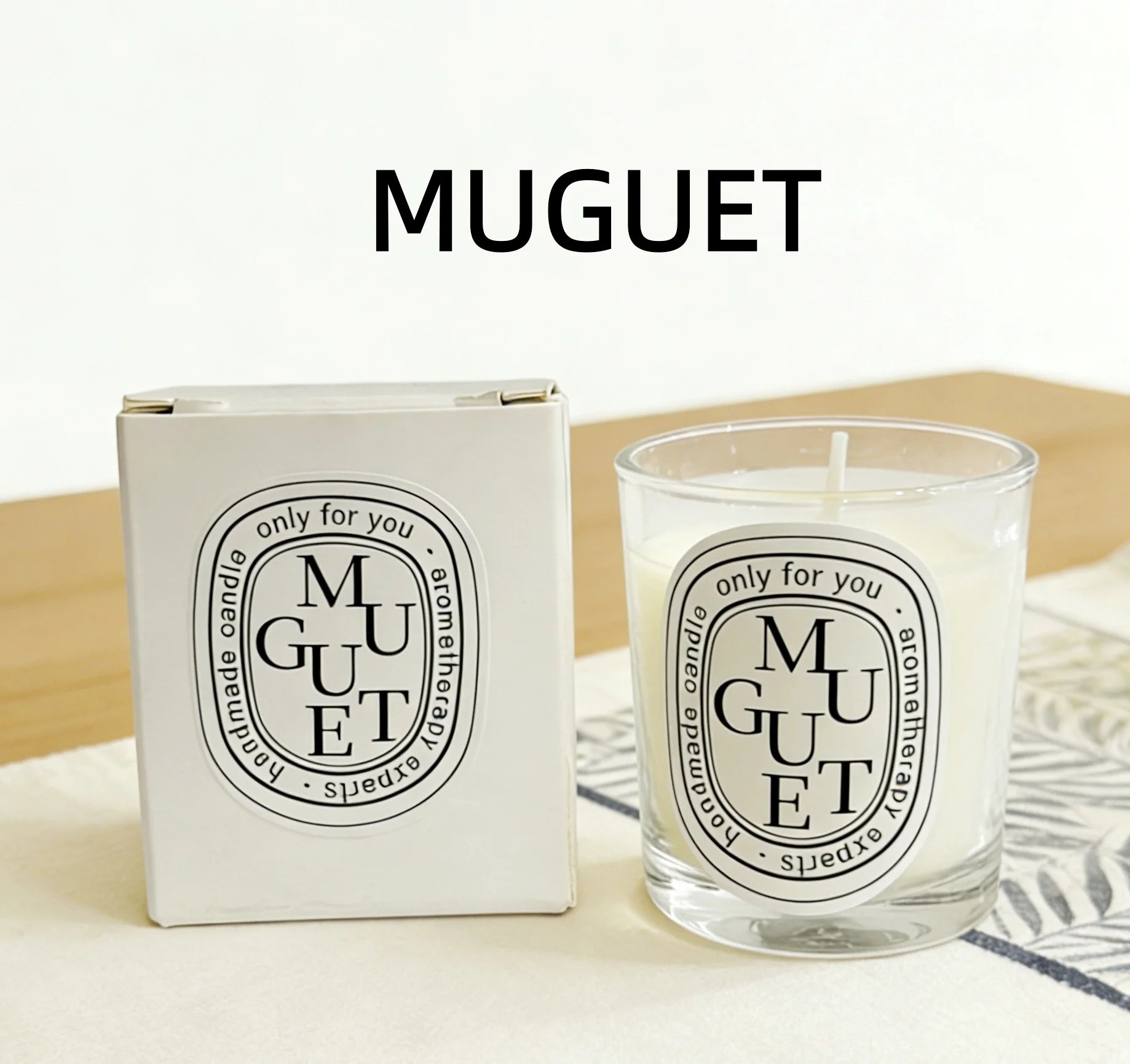 White aromatherapy scented candle in a glass holder with matching gift box, featuring Muguet branding.