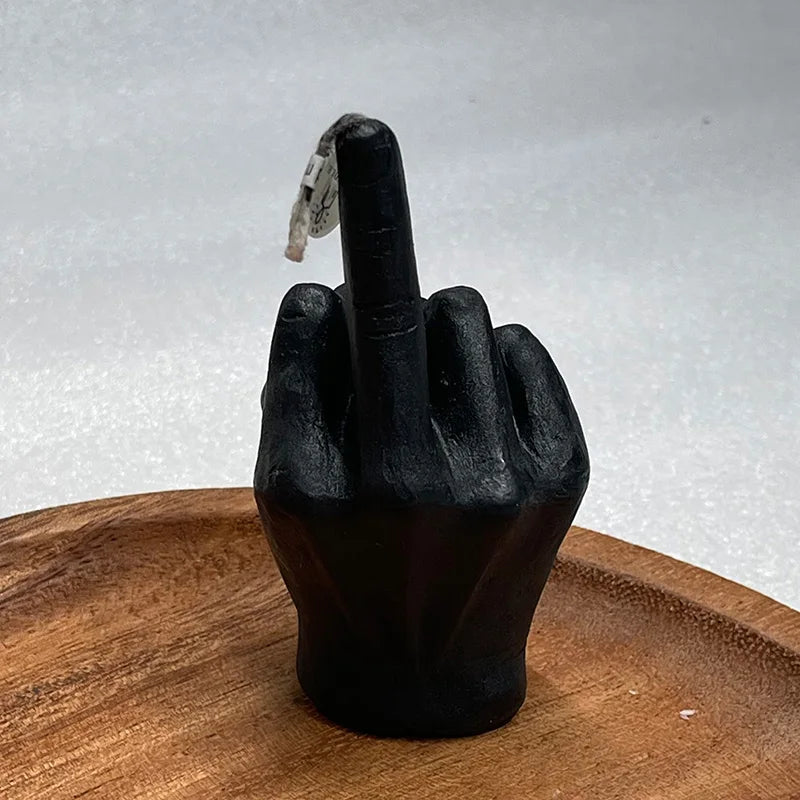 Black candle shaped like a hand giving the middle finger, resting on a round wooden tray.