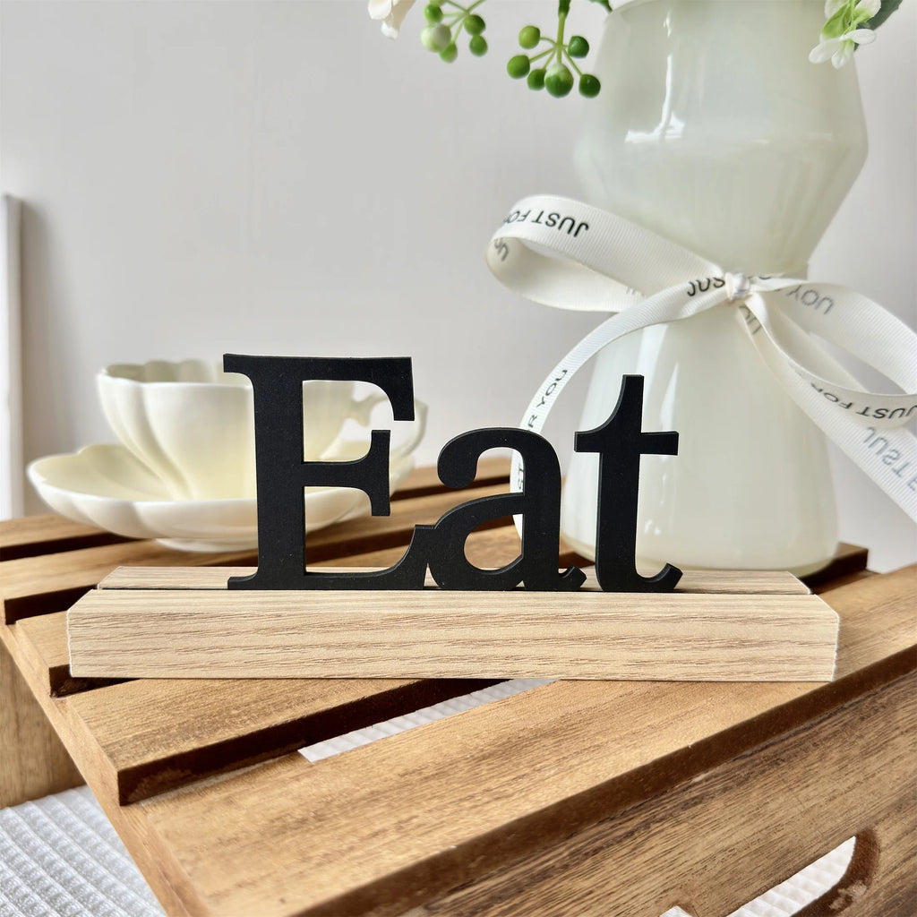 Black wooden "Eat" sign mounted on a natural light wood base, displayed on a rustic wooden crate.