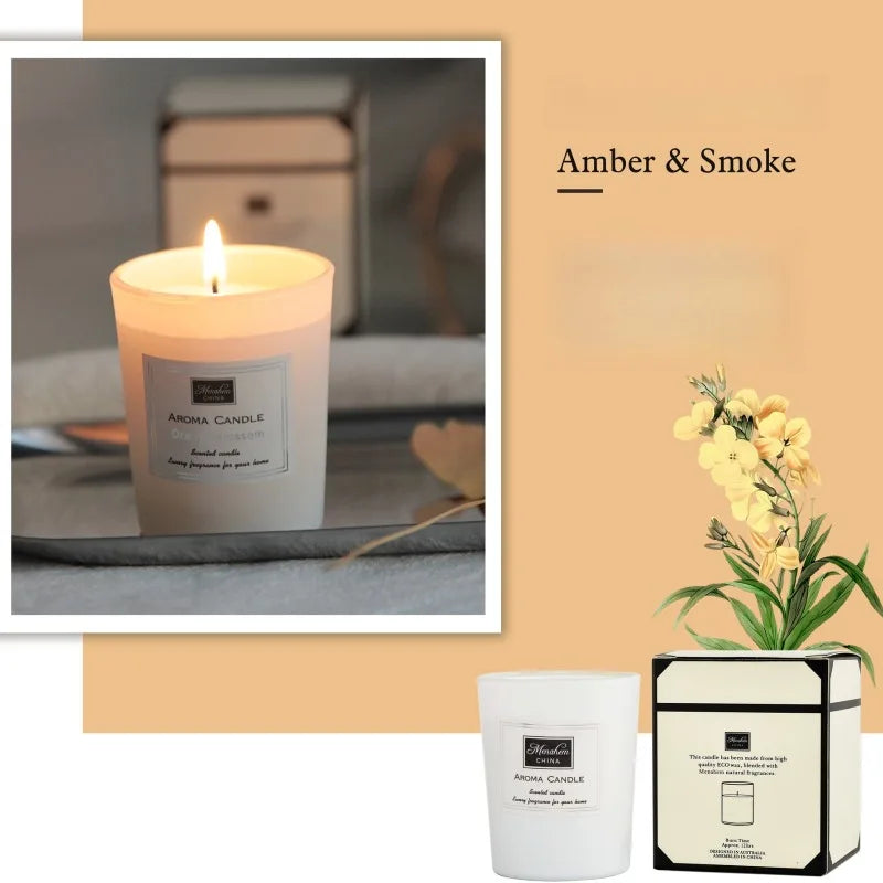 Lit Amber & Smoke scented candle in a minimalist white glass jar with a matching presentation box and floral accent.