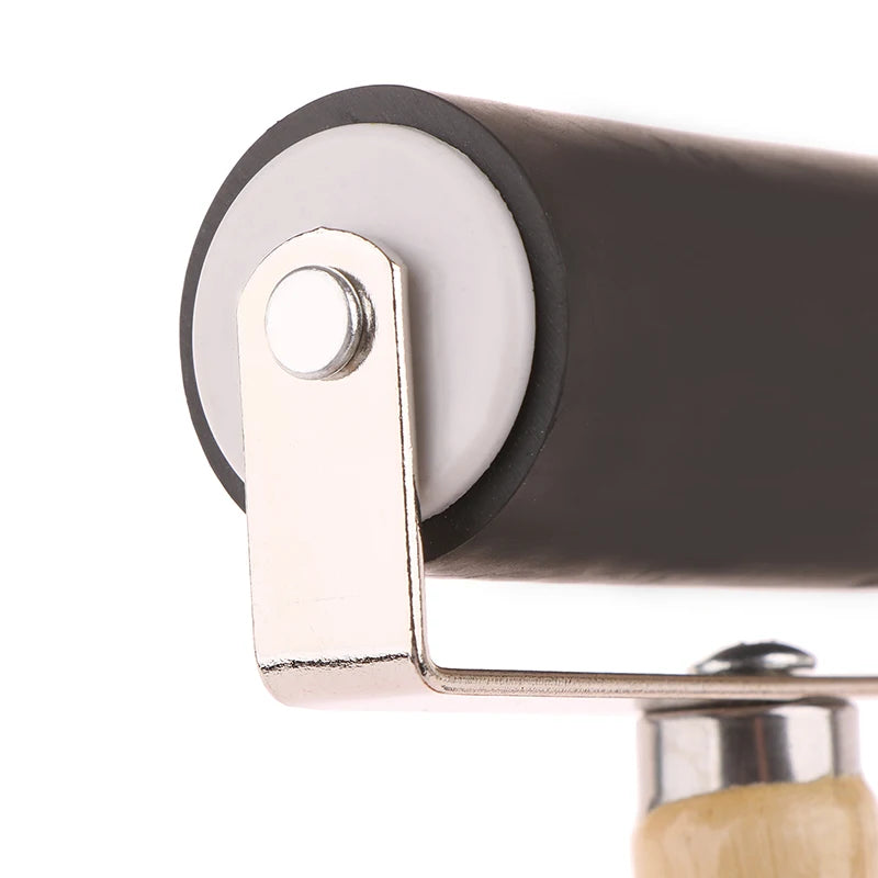 Close-up of a rubber craft brayer roller with a smooth black barrel, silver metal frame, and light wood handle.
